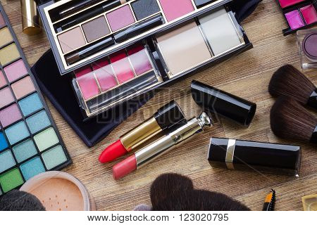 set of  brushes, lipsticks, maskara, eye shadows and  powder on wood