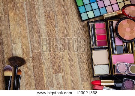 Frame of  brushes, lipsticks, maskara, eye shadows and  powder on wooden table, top view