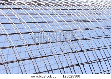 Metal grid of white alloy shines in bright sunlight on the blue sky background