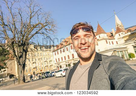 Young handsome man taking selfie at Meran old town in South Tyrol in Italy - Adventure and travel lifestyle around european destination - Composition with tilted horizon and warm afternoon color tones
