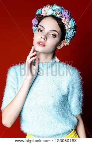 Beautiful model with a wreath of flowers on her head on red background. Beauty Woman face Portrait. Beautiful Spa model Girl with Perfect Fresh Clean Skin.