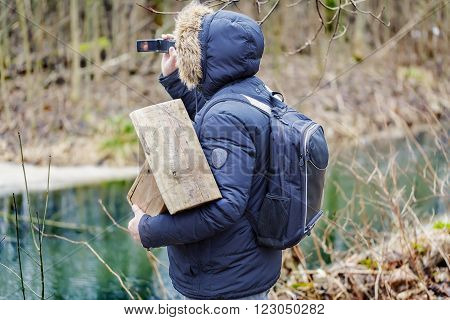 Ornithologist with camcorder and bird cage in the park near river