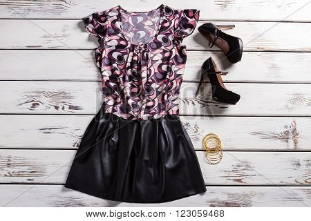Female clothes and heel shoes. Woman's trendy outfit on shelf. Dark outfit and yellow bracelets. Clothing and small bright accessories.