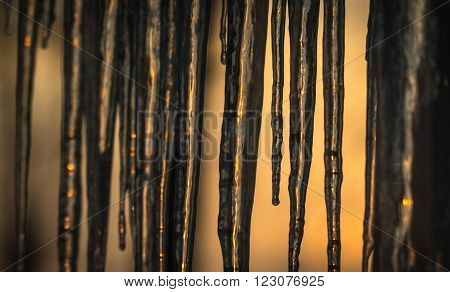 Abstract background of natural icicle formation through glass as morning sun rises.  Long icicles on a wintry January morning. Sunshine dawning through icicles that hang low from a roof's edge.