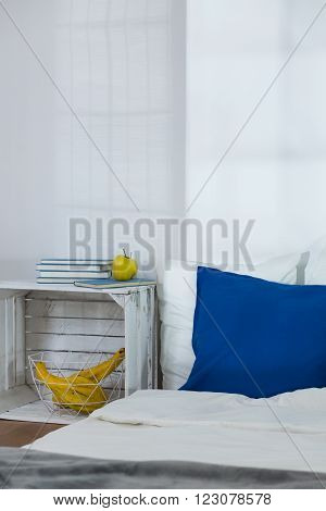 Simple cozy bedroom with white walls and mattress on floor. Stylish modern nightstand made of wooden box