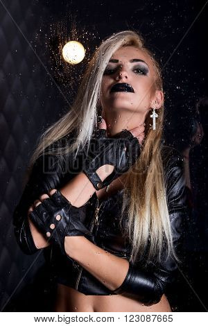 Portrait of pretty sexy young woman in leather jacket with water drops and flash light. Water studio photo.