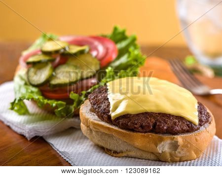 Open face cheeseburger with lettuce, tomato, onion, and pickle garnish on a napkin sitting on a wooden table top.