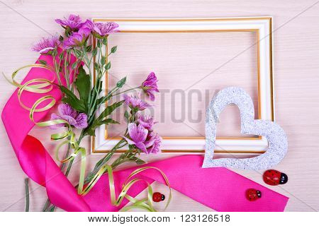White frame and purple flowers with a red ribbon on the wooden background