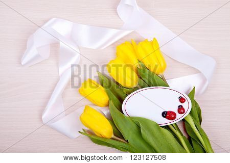 Bouquet of yellow tulips and a card to test with ladybirds on a wooden background. Congratulation to the holiday. Card