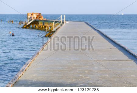 Higgs Beach Pier in Key West sticking out in the ocean with ladders leading into the water. Some people are sitting and standing on the pier or swimming next to it