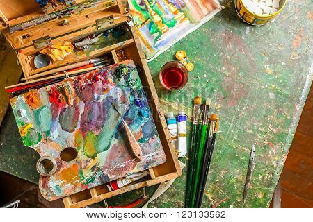 Bright workplace of the artist with brushes, oil paints, pallete, palette knife and tea with lump sugar