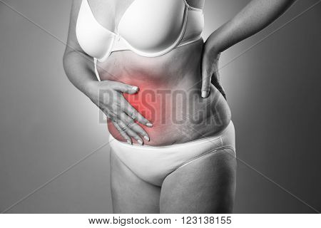 Woman in a white bra and white panties with abdominal pain on a gray background. Black and white photo with red dot