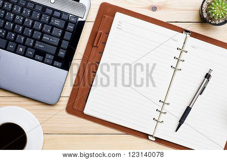 Blank leather notebook with pen cup of coffee and labtop on office desk.Top view