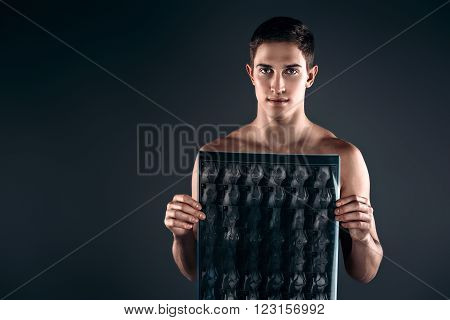 Studio shot of handsome young man with naked torso. Muscular man looking at camera and holding X-ray photo