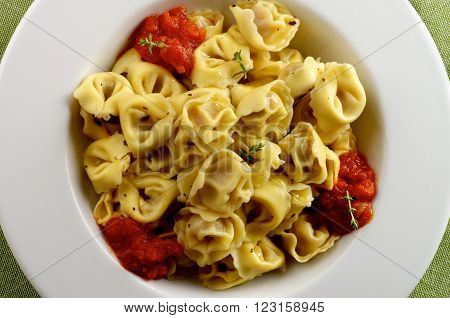 Delicious Meat Cappelletti in with Tomatoes Sauce in White Plate closeup on Green Napkin background