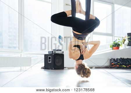 Back view of attractive young woman doing antigravity yoga using hammock in studio
