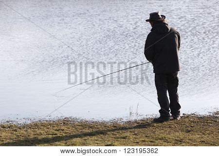 silhouette of lonely fisher with fishong rod near water