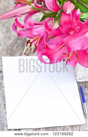 Pink lily Robina flowers bouquet and blank paper sheet with pen on rustic wooden table