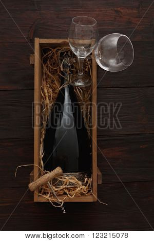 Bottle of red wine in wooden crate filled with straw next to to empty glasses with corkscrew on wooden table. Flat lay, above view, copy space,Chiaroscuro styled