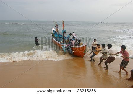 MARAVANTHE, KARNATKA/INDIA - MAY 25 2014: 
Fishermen join together to pull their boat into the shore after arriving  with the catch May 25, 2014 in Marvanthe, Karnataka, India.