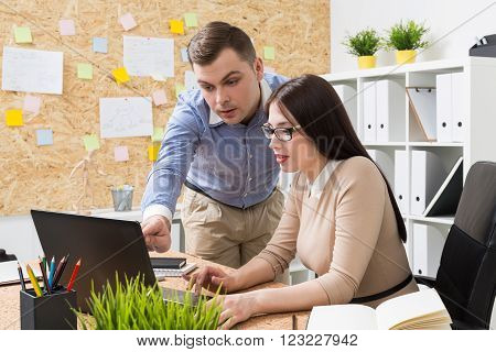 Woman in glasses working at computer,  man standing next to her and showing something on scren. Office. Concept of work.
