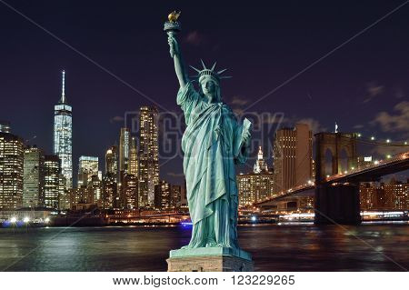 Manhattan skyline with Brooklyn Bridge at night and Statue of Liberty.