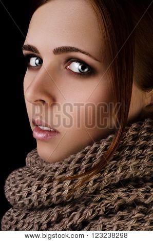 Portrait of a young girl in a scarf-snood large knitting on a black background