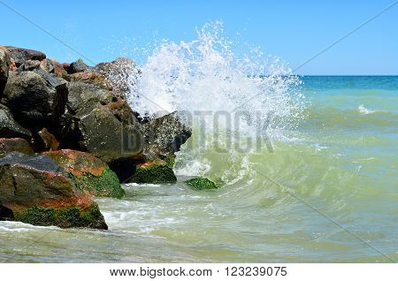Waves splash on the large boulders on the beach