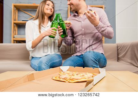 Man And Woman Eating Pizza And Clinking With Bottles Of Beer