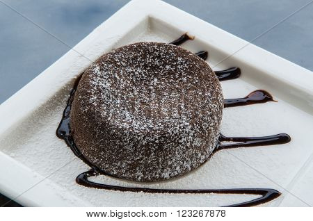 Chocolate lava cake topped with chocolate cream on a white plate.