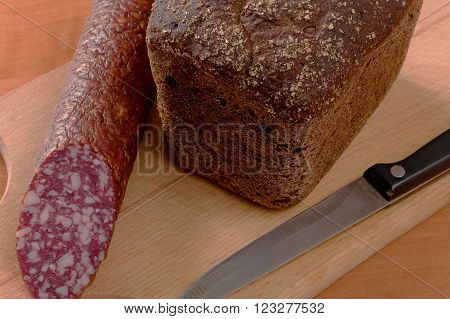 Sausage sliced with a knife on a wooden table. Fresh rye bread and sausage on wooden table