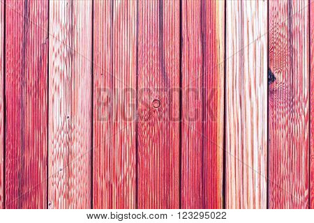 A fragment of an old wooden fence. Painted wooden planks as a background with copy space. Wooden rustic background or painted wood boards texture. Old peeling red paint.