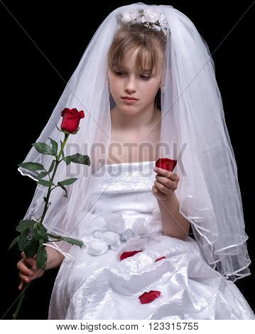 Very young bride. Wedding white dress. Luxury veil. Flower red rose. Background black. Bride sad. A minor child. The concept of the wedding teens