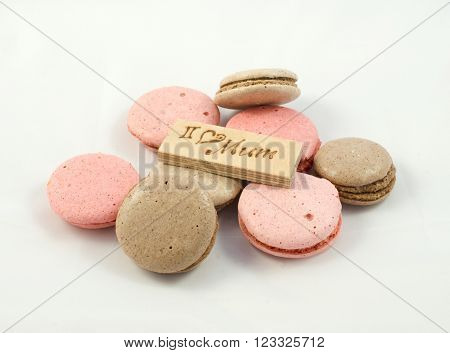 Chocolate and pink macarons chaotically arranged and a board with the inscription I love mum. A Happy Mother's Day theme.