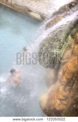 People in the pool standing under a waterfall jets with healing thermal spring water.