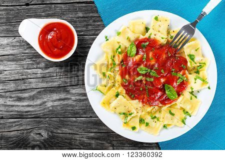 Italian ravioli filled with ricotta cheese and spinach with tomato sauce and basil leaves sprinkled with freshly ground black pepper on a white dish on an old rustic background top view
