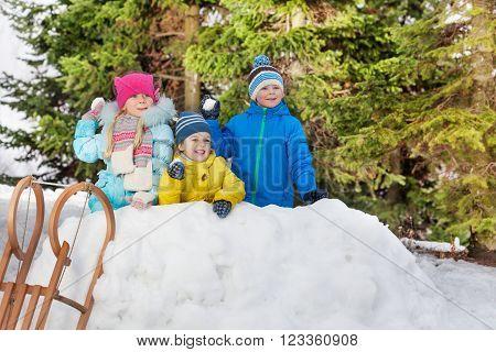 Group of little children in snow fortress throw snowballs