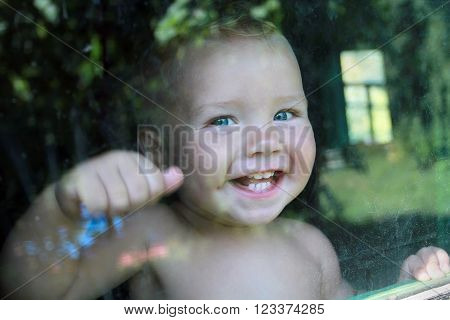 Very emotional little blue-eyed boy happily knocking on the window.