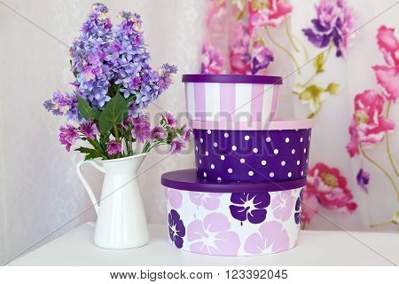 Bouquet branches purple lilac in a white vase on a table and a set of gift boxes in room