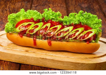 Hot dog. American fast food restaurant cuisine - spicy chili hotdog with mustard, mayonnaise and ketchup with lettuce at wooden desk on the table. Chili hotdog at wood.