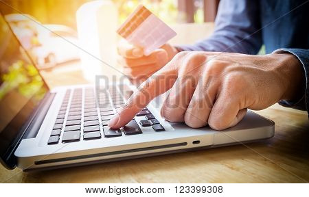 Man holding credit card in hand and entering security code using laptop keyboard.