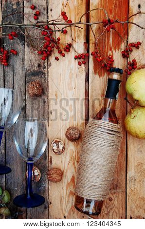 The still life with white wine in glass bottle on wood background. Glasses of wine with fresh grapes. Bottle and footed glass. Fresh ripe white grapes walnuts juicy ripe pear. Drink. Rustic style.