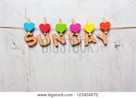 Sunday word from wooden letters with colored clothespins on a white wooden background