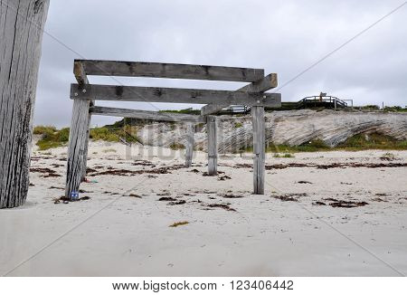 Old jetty ruins in Hamelin Bay, Western Australia with limestone cliffs, vegetated dunes and wooden boardwalk under dark stormy skies.
