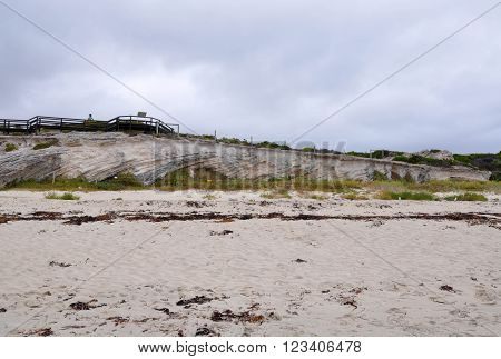 Hamelin Bay beach in Western Australia with limestone cliffs, vegetated dunes and wooden boardwalk under overcast skies.