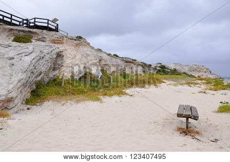 Coast line of Hamelin Bay, Western Australia with limestone cliffs, resting bench and wooden boardwalk overlook under dark stormy skies.