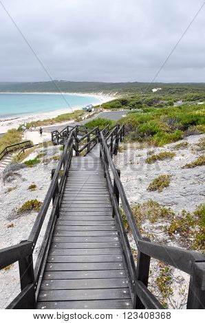 Wooden boardwalk overlooking the turquoise Indian Ocean seascape at Hamelin Bay beach with limestone rock and vegetated dunes under dark, stormy skies in Western Australia.