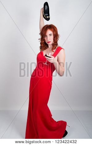 Beautiful young sexy slim red-haired girl wearing a silk red dress high heels, in alcoholic intoxication. drinking red wine from a glass. after party.