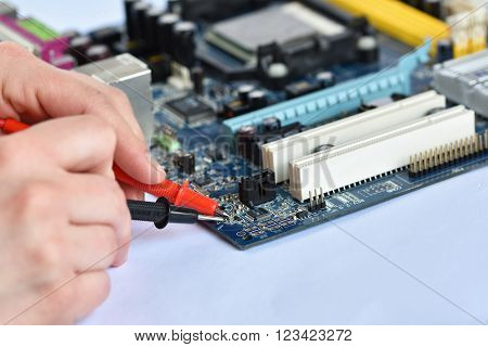 Hand with voltmeter above board with components. Repair of computers and modern technologies.