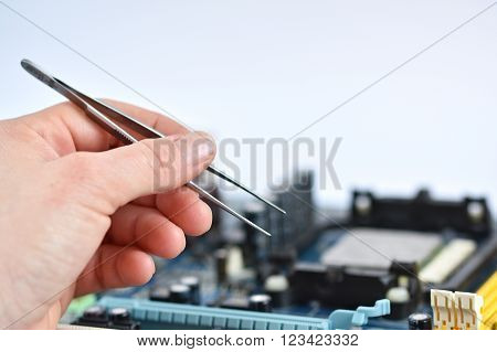 Hand with tweezers above board with components. Repair of computers and modern technologies. PCB.